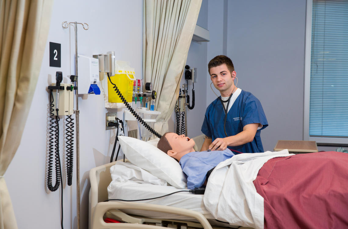 Mackenzie Margetts, president of the Nursing Guys Club, examines a patient in a simulation lab.